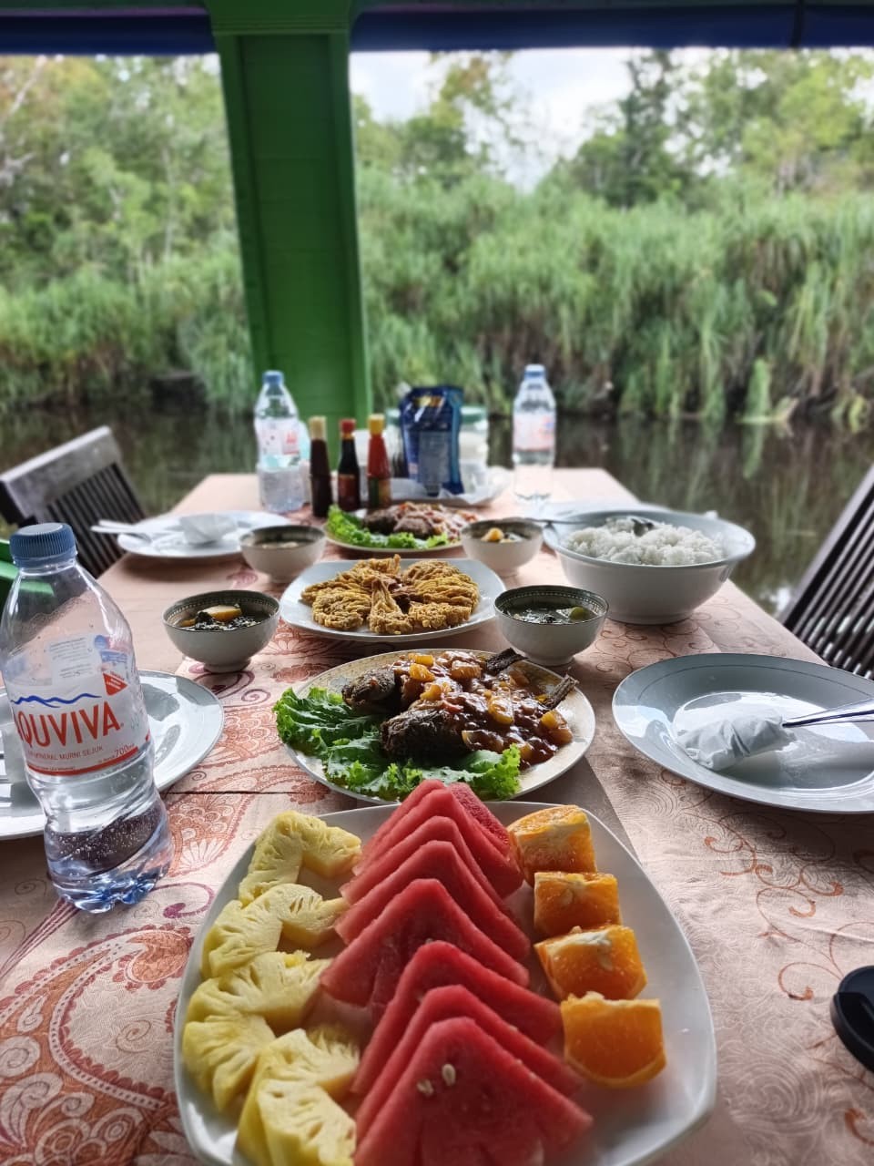 Semangka, nanas, dan pepaya segar bersama hidangan makan siang lengkap di klotok tepi sungai.