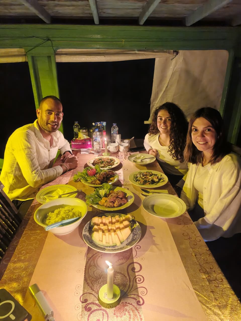 Makan malam romantis dengan lilin di klotok dengan hidangan Indonesia lengkap disajikan di malam hari.